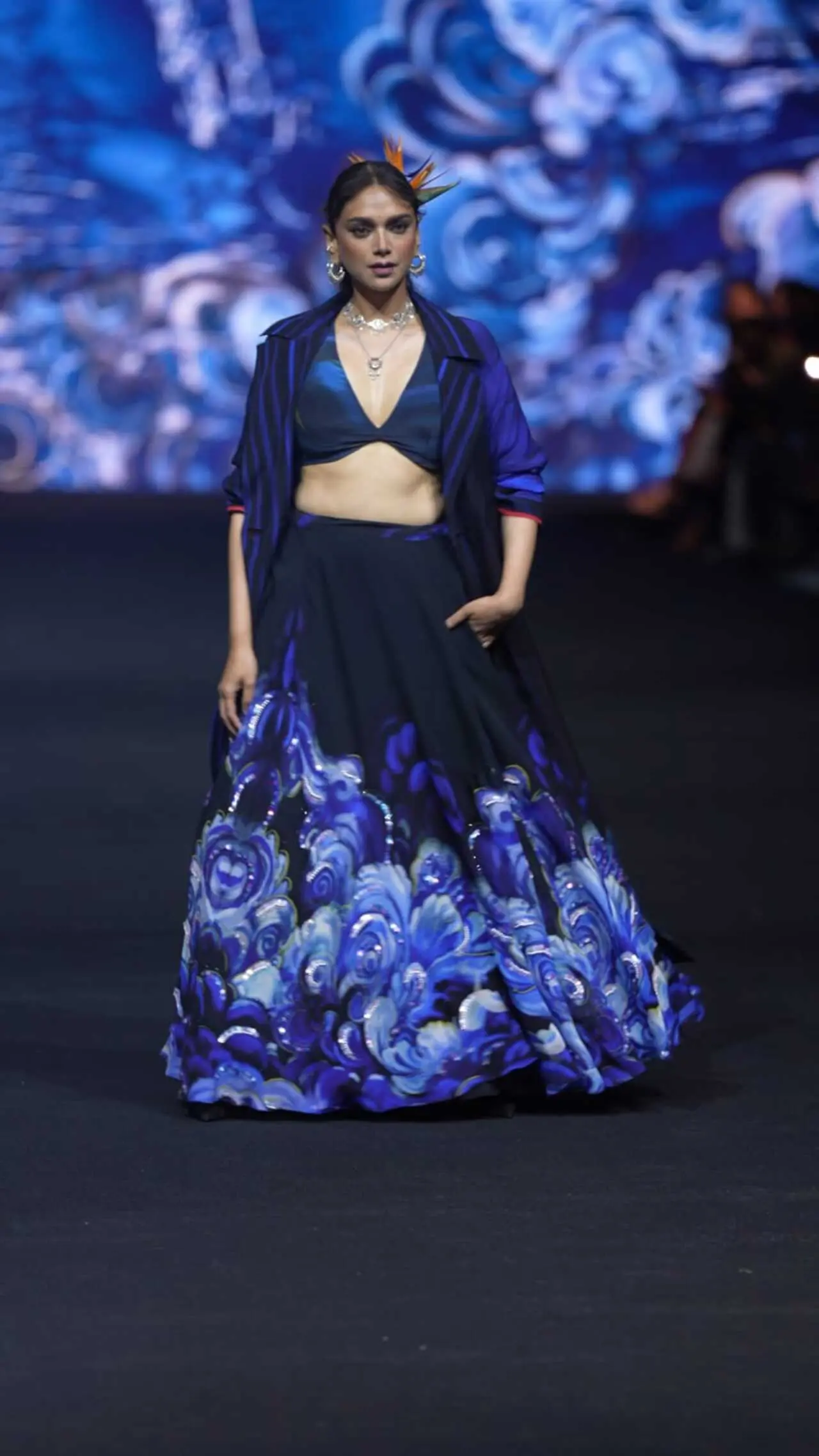 Aditi Rao Hydari stuns on the runway in a deep blue ensemble featuring a flowy printed skirt and a matching bralette. She layers it with a structured jacket, adding a bold and contemporary edge to the look.